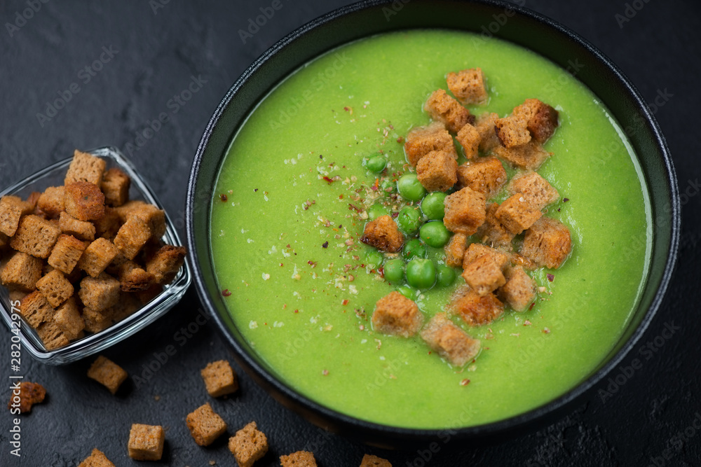 Bowl of cream-soup with green peas and croutons on a black stone background, close-up Bowl of cream-soup with green peas and croutons on a black stone background, close-up