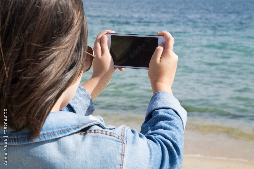 Girl taking picture with the mobile phone of the beach and the sea