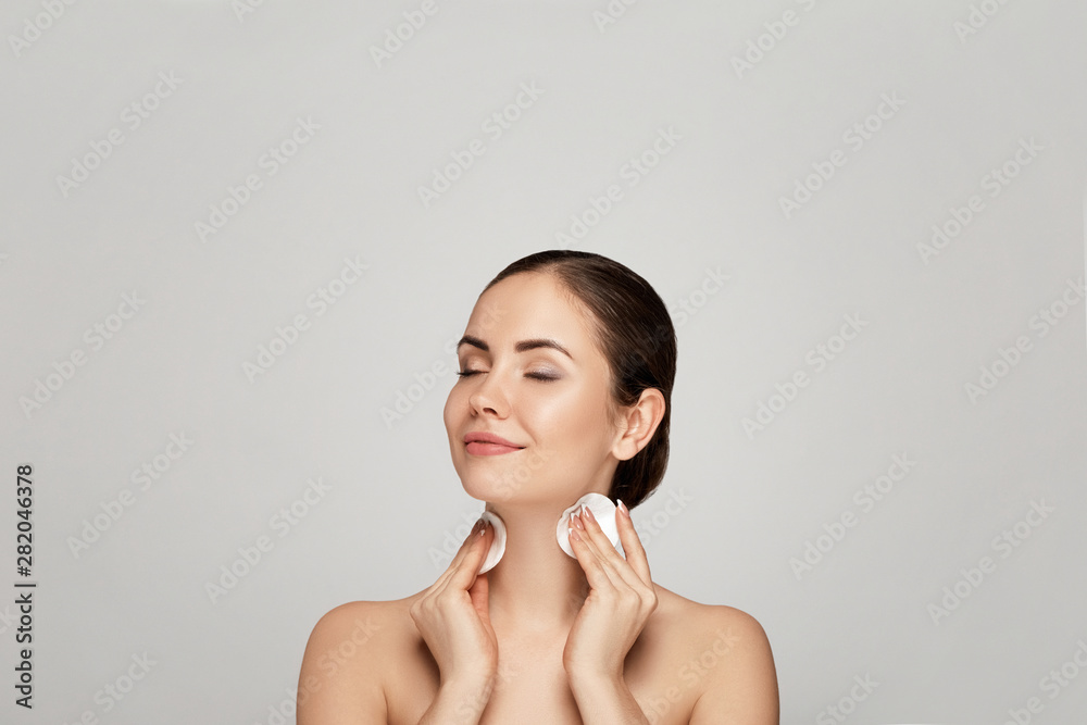 Obraz premium Beauty portrait of a cheerful young topless woman removing face make-up with a cotton pad