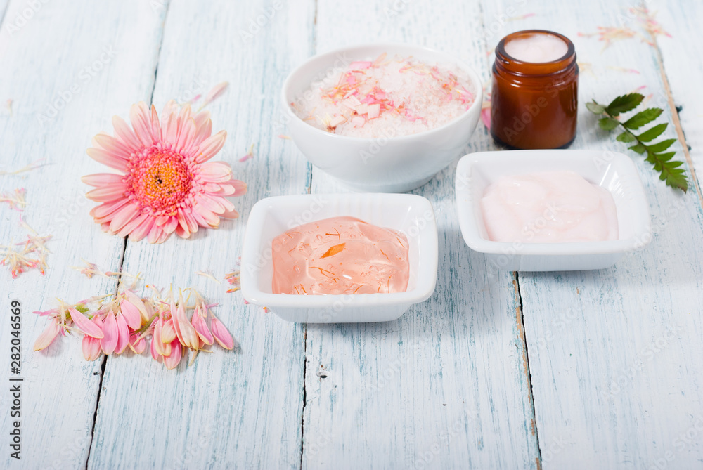 beauty product samples, cosmetic cream, bath salt, liquid soap and pink flower, white wood table