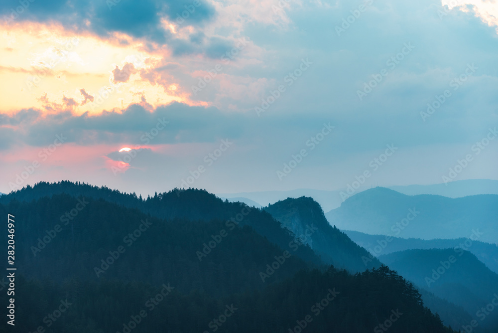 Beautiful dramatic sunset in the mountains. Landscape with sun light shining through orange clouds