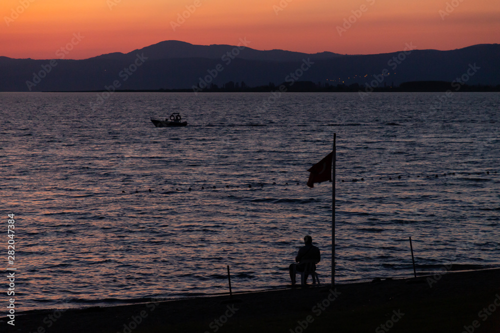 boat, flag and person silhouetted at sunset on Lake Iznik, Turkey