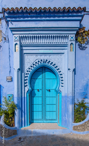Typical, old, blue intricately carved, studded, Moroccan riad door and door-frame and old house. Beautiful view of the blue city in the medina. painted houses in CHEFCHAOUEN, MOROCCO © mitzo_bs