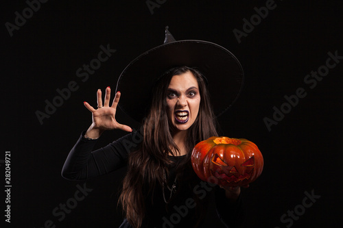 Gothic young woman in witch halloween costume standing over black background