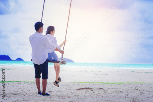 Romantic couple relaxing together on rope swing at the beach, Love and honeymoon concept.