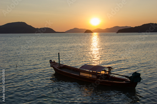 Colorful Sunset on Phuket Island in Thailand. This photograph was taken at a beach in Panwa. It shows the mountains and a traditional boat in the image.