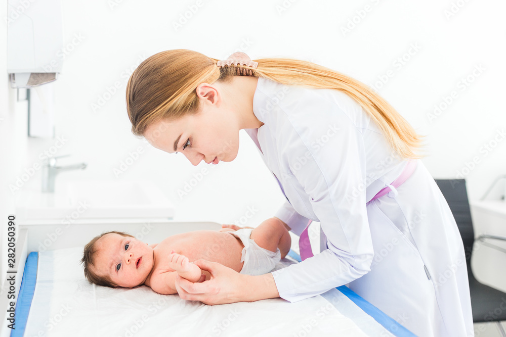 Beautiful young female blonde pediatrician doctor examines baby girl checking her skin Beautiful young female blonde pediatrician doctor examines baby girl checking her skin
