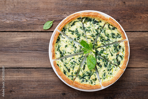 Vegetarian spinach pie or tart with feta cheese on wooden background.