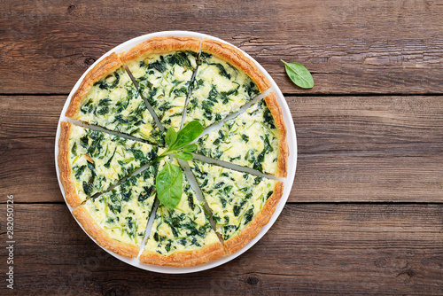 Vegetarian spinach pie or tart with feta cheese on wooden background.