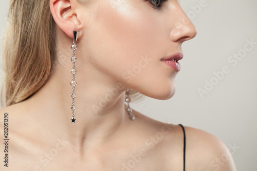 Closeup face of beautiful woman wearing silver earrings with diamonds on white background, elegant female profile