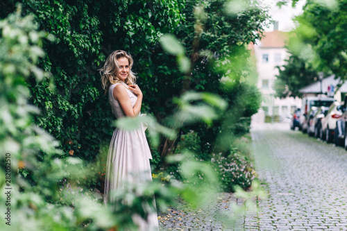 Wallpaper Mural A blonde girl of European appearance in an evening dress poses in a city park on a background of green bushes and trees Torontodigital.ca