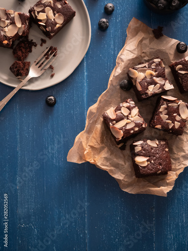 Homemade chocolate brownies with almond slices topping and blueberries on blue wooden table