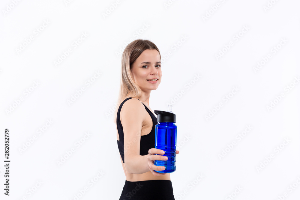 Young sporty blond woman in a black sportswear with smart watches holds bottle with water after workout standing over white background. Young sporty blond woman in a black sportswear with smart watches holds bottle with water after workout standing over white background.