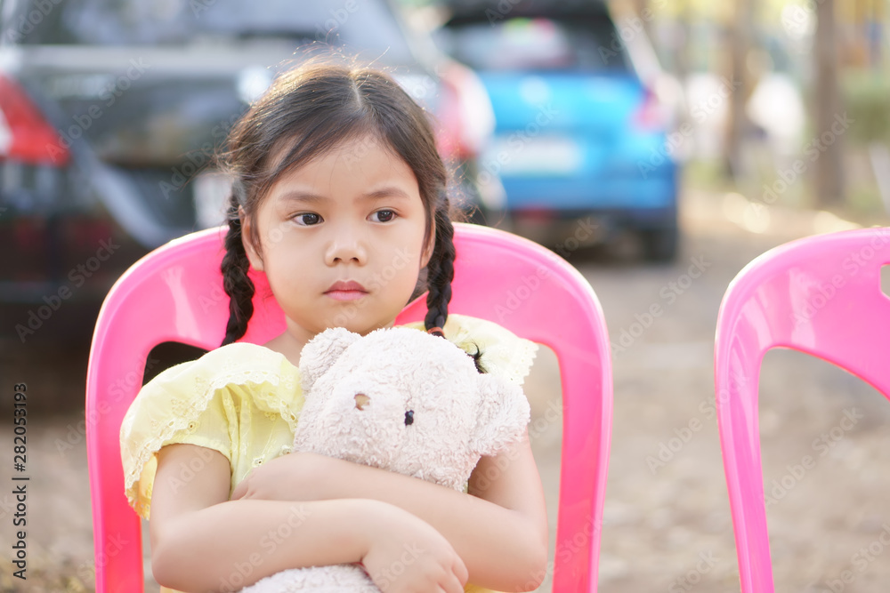 Asian child cute or kid girl pigtail sad with miss and lonely with hug teddy bear doll to lovely toy on street or city park with car and vacant sit on pink chair Asian child cute or kid girl pigtail sad with miss and lonely with hug teddy bear doll to lovely toy on street or city park with car and vacant sit on pink chair