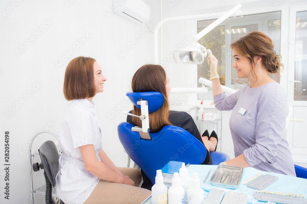 a woman dentist with an assistant treats a tooth to a woman in a modern dental clinic a woman dentist with an assistant treats a tooth to a woman in a modern dental clinic