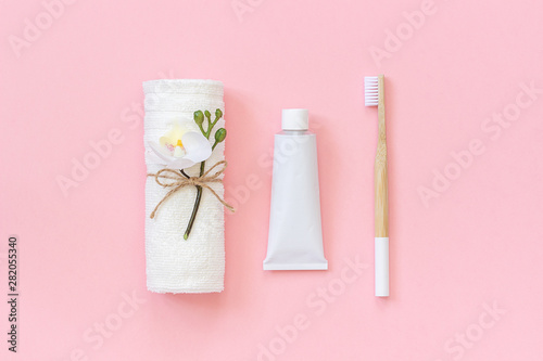 Natural eco-friendly bamboo brush, white towel and tube of toothpaste. Set for washing and brushing your teeth on pink background. Template for design Top view Flat lay