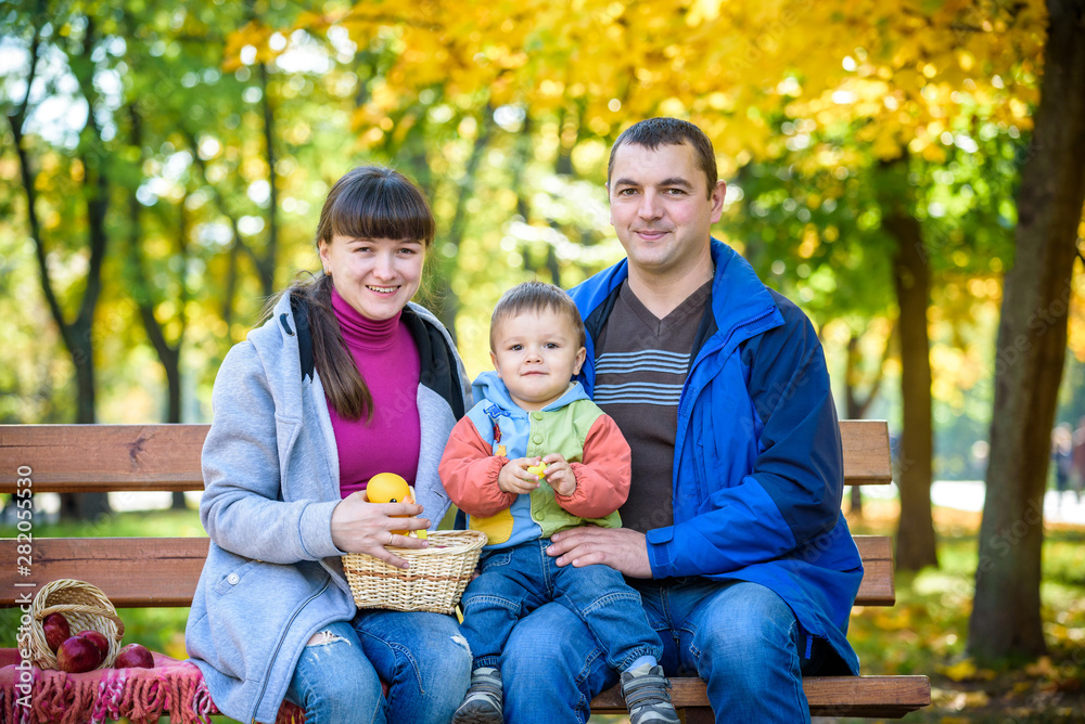 Fototapeta premium happy family enjoying autumn picnic. Father mother and son sit on bench with apples basket. Happy family leisure together concept