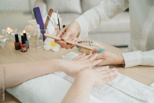 Manicure process at home service. focus on hands of two young asian women worker and customer in living room. Doing manicure nail file by wooden brush to clean up finger on table with candles beside.