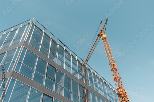 Slika na platnu the corner of the new glass wall of an office building and yellow construction crane against a clear blue sky