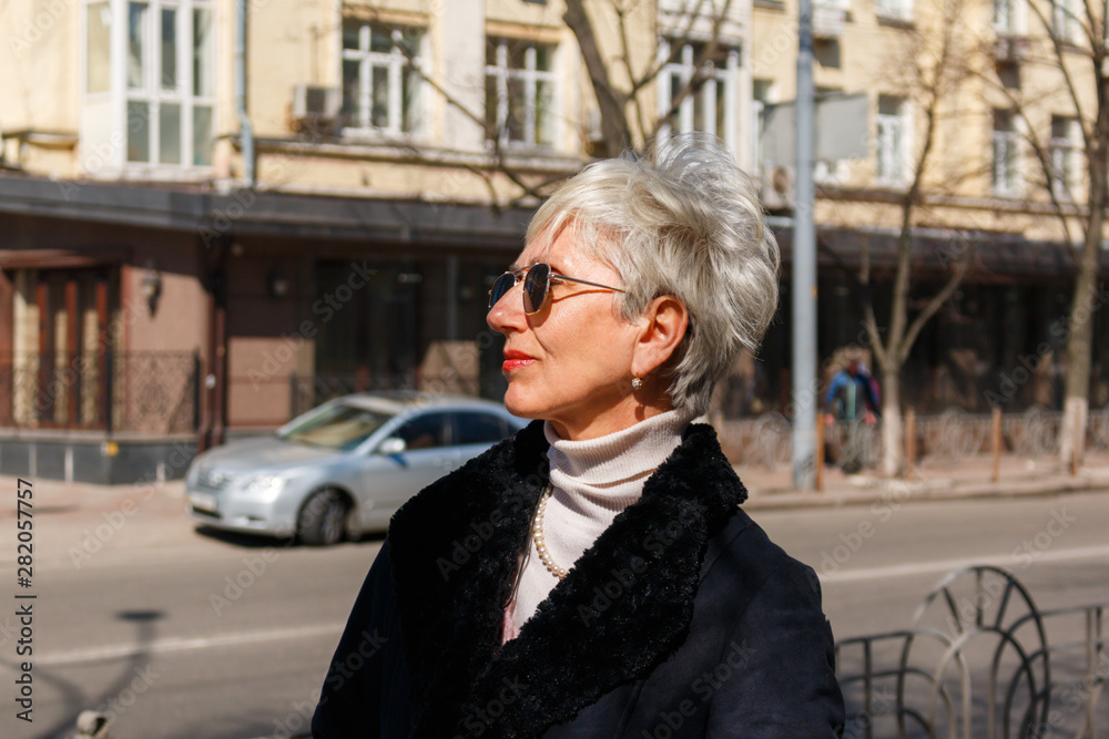 beautiful gray-haired lady in sunglasses stands on the street near the road, city background, profile portrait. fashionable middle-aged woman photographed in profile on the street. beautiful gray-haired lady in sunglasses stands on the street near the road, city background, profile portrait. fashionable middle-aged woman photographed in profile on the street.