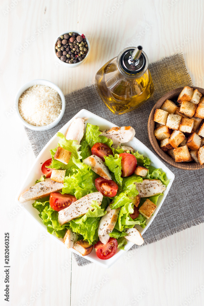 Fresh salad made of tomato, ruccola, chicken breast, eggs, arugula, crackers and spices. Caesar salad in a white, transparent bowl on wooden background Fresh salad made of tomato, ruccola, chicken breast, eggs, arugula, crackers and spices. Caesar salad in a white, transparent bowl on wooden background