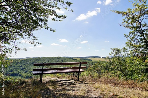 empty bench on a hill in a forest landscape. bench , mountains at horizon. Empty wooden bench on the hill under bended tree with sky background. peaceful, emptiness, loneliness and relax concept. 