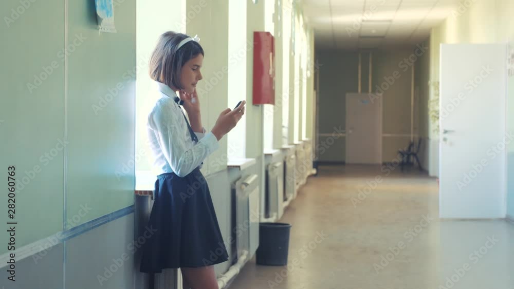 schoolgirl education with smartphones at school concept lifestyle . Young girl teen and using smartphone standing by the window in the corridor of the school. correspondent in the messenger, write a schoolgirl education with smartphones at school concept lifestyle . Young girl teen and using smartphone standing by the window in the corridor of the school. correspondent in the messenger, write a