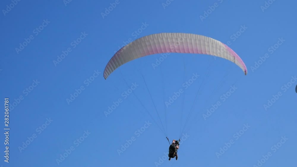 Extreme paraglider flying against a clear blue sky, sunbeam shines into camera. Paraglide flight experience skydive summer. Extreme vacation Extreme paraglider flying against a clear blue sky, sunbeam shines into camera. Paraglide flight experience skydive summer. Extreme vacation