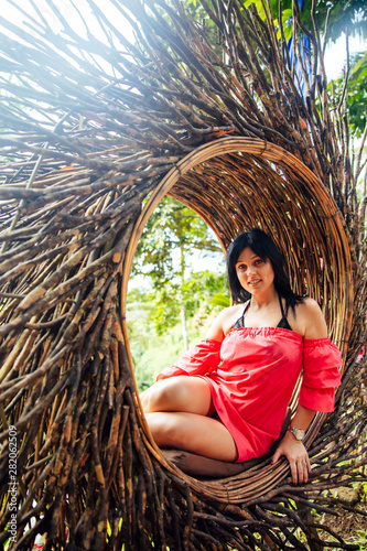 A female tourist is sitting on a large bird nest on a tree at Bali island
