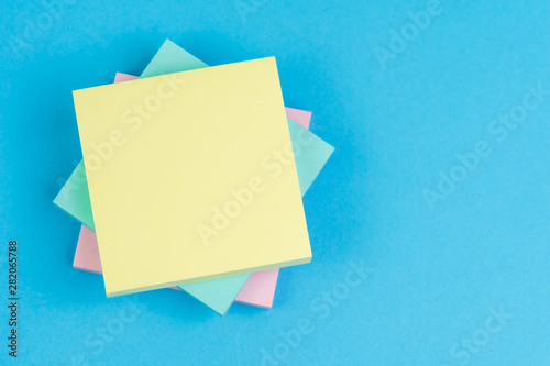 Stack of sticky notes on solid blue background with pink, blue and yellow on top with copy space for writing message using as memo, reminder or business idea and important quote