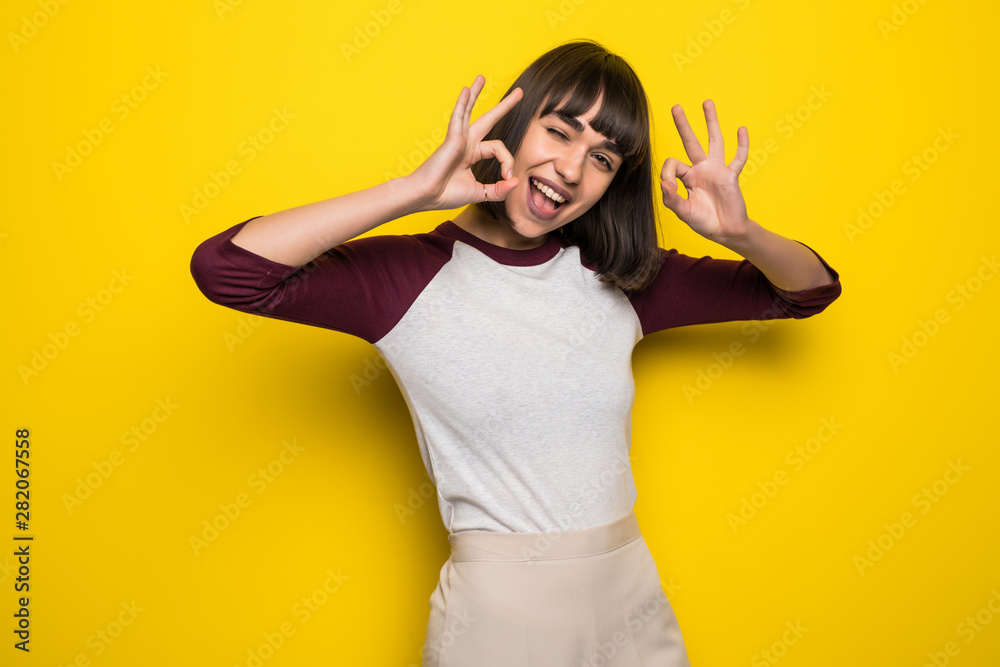 Fototapeta premium Portrait of a cheerful happy pleased young pretty woman showing okay gesture posing isolated over yellow wall background.