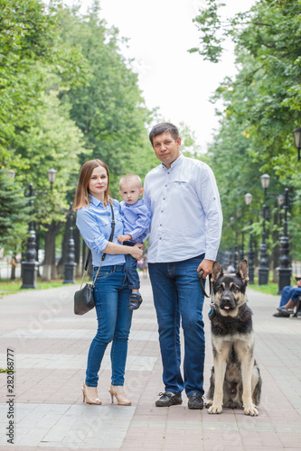 Family walk: mom, dad and son with his dog in a city park for a walk. The baby is in the arms of the mother. German shepherd is the best friend of the child. © izida1991
