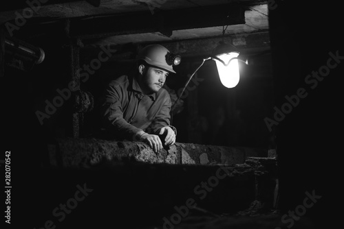 A young guy in a protective suit and helmet sits in a tunnel with a burning scrapbook. Miner in mine