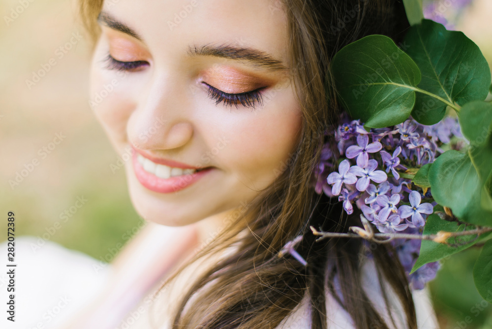 Beautiful young cute girl with professional makeup close up and dazzling white smile with lilac flowers happy Beautiful young cute girl with professional makeup close up and dazzling white smile with lilac flowers happy