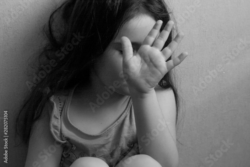black and white portrait of emotional angry little girl closing her face with her hand who doesn't want to talk
