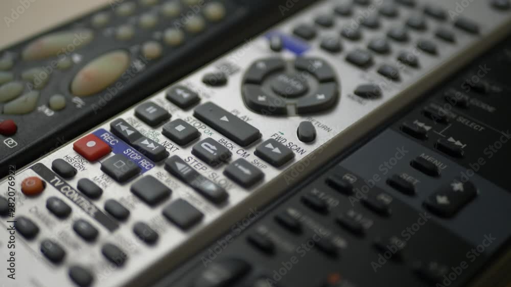 Black and silver different TV remote controls with buttons are on table Black and silver different TV remote controls with buttons are on table