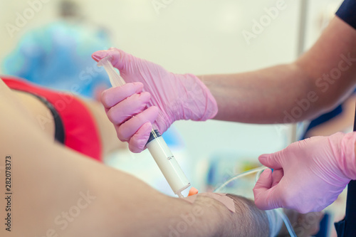 Preparation for surgery. Medical nurse with pink latex gloves inputs catheter to vein patient for drip of chemotherapy or another liquid medicine, jection of propofol to patient for iv anesthesia.