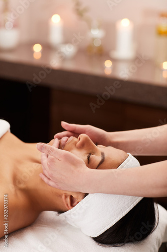 Head and shoulders portrait of beautiful mixed-race woman enjoying face massage in luxury spa, copy space