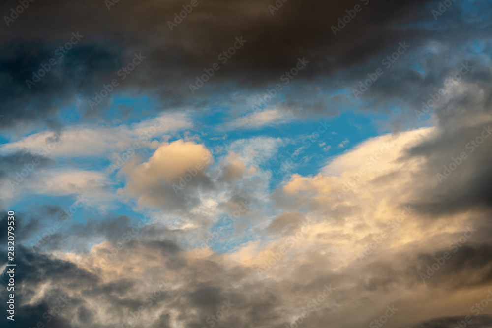 Golden fluffy clouds illuminated by disappearing rays at sunset and dramatic dark thunderclouds floating across sunny blue sky to change summer weather. Stunning view natural meteorology background. Golden fluffy clouds illuminated by disappearing rays at sunset and dramatic dark thunderclouds floating across sunny blue sky to change summer weather. Stunning view natural meteorology background.