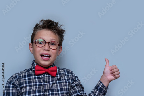 Young boy giving thumbs up portrait on violet background. Child enjoying  approving of something. Happy kid in red bowtie and checkered shirt giving likes. Fun  cheerful pastime  activity for children