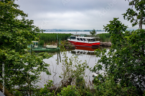 IOANNINA, GREECE - JUNE 6, 2019 - Small tourist cruise white and red and green fishing boats moore on lake Pamvotida near the beautiful small Greek town. Early morning spring view with unusual fog photo