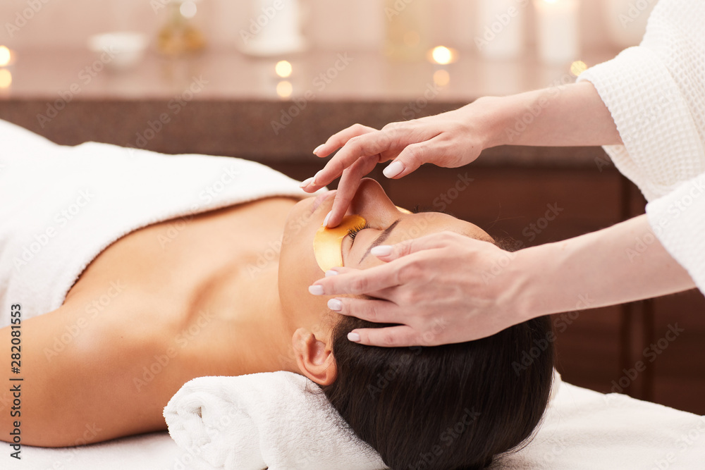 Naklejka premium Portrait of beautiful woman enjoying facial therapy while lying on massage table in luxury spa, copy space