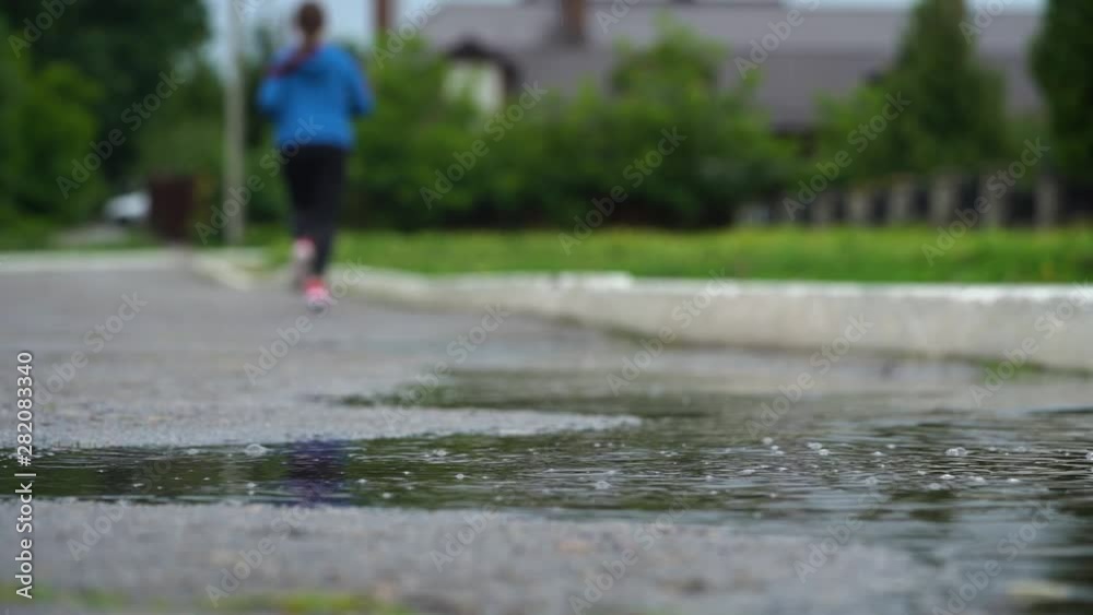 Legs of a runner in sneakers. Sports woman jogging outdoors, stepping into muddy puddle. Single runner running in rain, making splash Legs of a runner in sneakers. Sports woman jogging outdoors, stepping into muddy puddle. Single runner running in rain, making splash