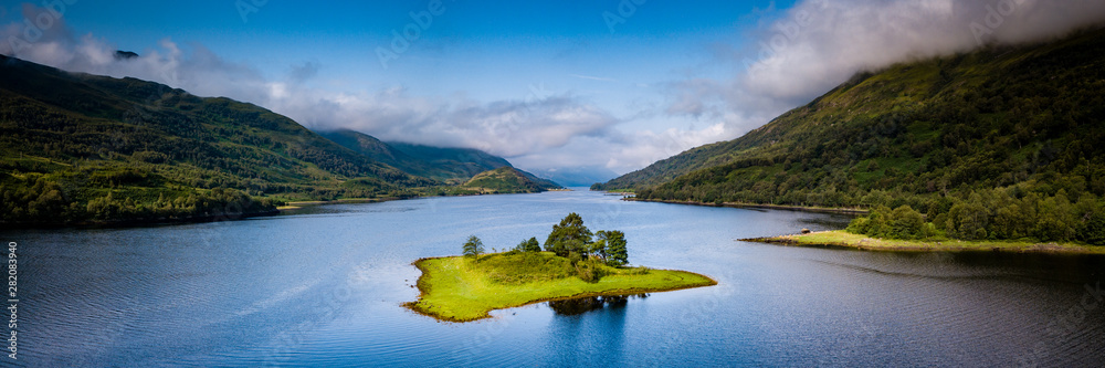 aerial view of loch leven near kinlochleven and glen coe in the argyll region of the highlands of scotland with a green island in the foreground and calm blue waters with misty mountains