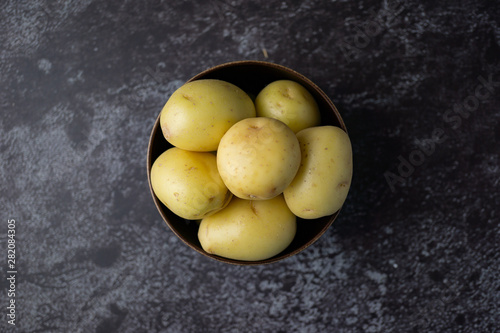Raw potatoes in a bowl on dark background. Selective focus.