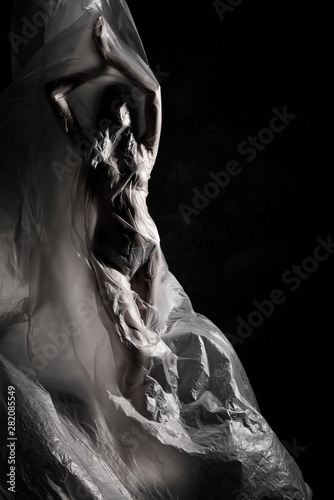 Billede på lærred Slim girl dressed only in underwear emotionally posing, wrapped in fluttering in the wind and fitting her graceful young body cellophane film