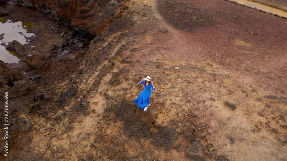 Aerial view of woman in a beautiful blue dress and hat stands on top of a mountain in a conservation area on the shores of the Atlantic Ocean. Tenerife, Canary Islands, Spain Aerial view of woman in a beautiful blue dress and hat stands on top of a mountain in a conservation area on the shores of the Atlantic Ocean. Tenerife, Canary Islands, Spain