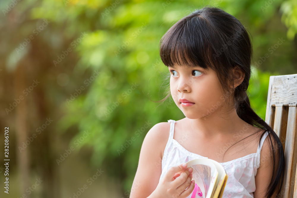 Cute Asian girl looking outside while sitting and reading book in Park Cute Asian girl looking outside while sitting and reading book in Park