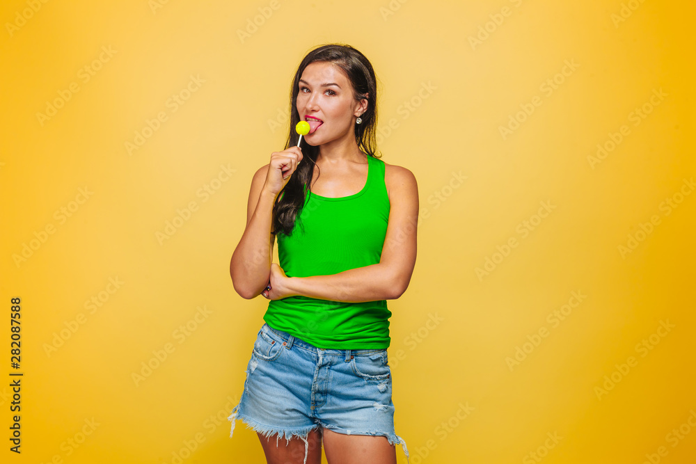 Girl on yellow background in green t-shirt eating Lollipop Girl on yellow background in green t-shirt eating Lollipop