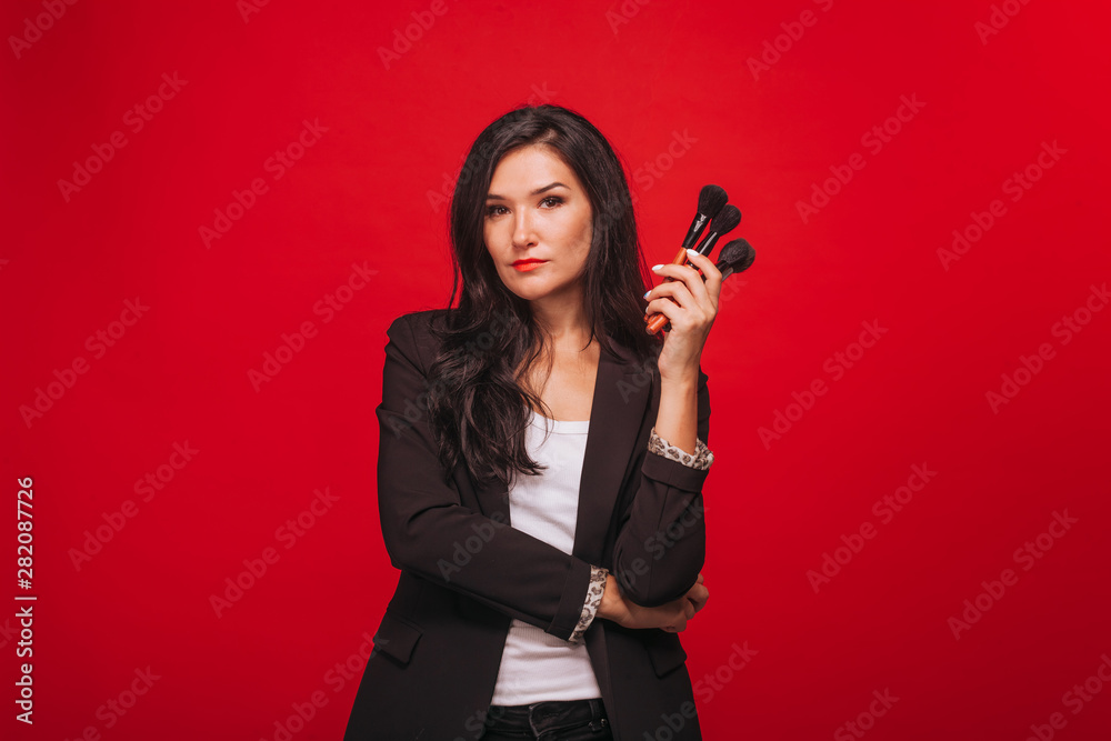 Girl holding makeup brushes on red background Girl holding makeup brushes on red background